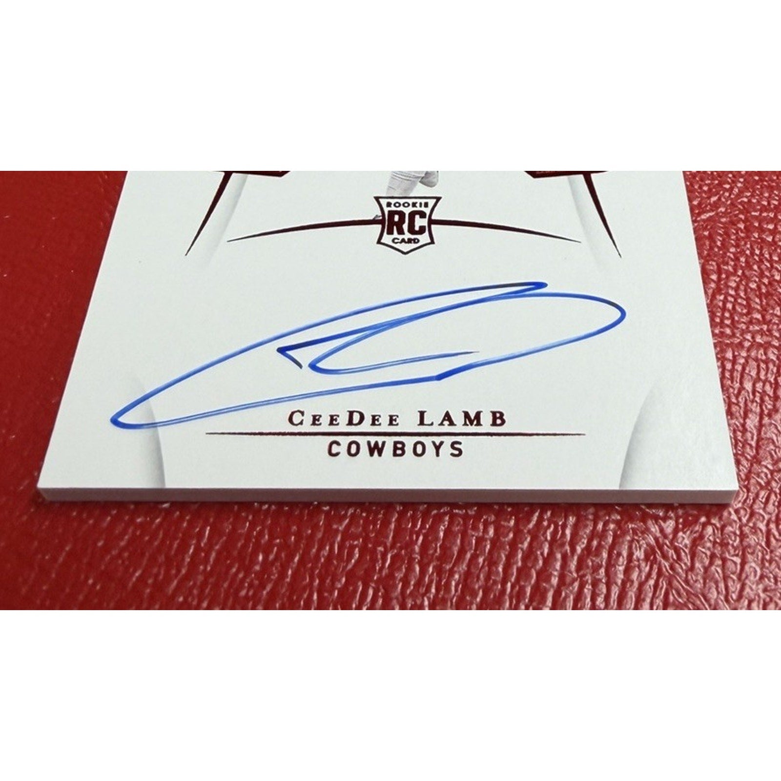 Card with a signature on it, featuring the name 'CeeDee Lamb' and 'Cowboys' text, on a red textured background.