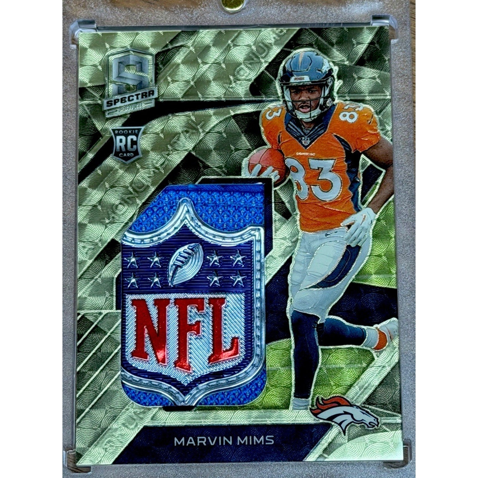Close-up angled front view of the Marvin Mims NFL Shield patch card showing the oversized NFL logo shield patch and Gold Vinyl finish